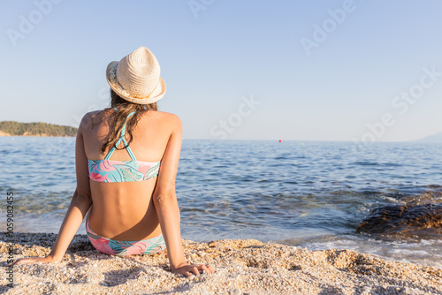 A young girl in a straw hat relaxes on a sunny beach, enjoying the warm weather and peaceful waves.