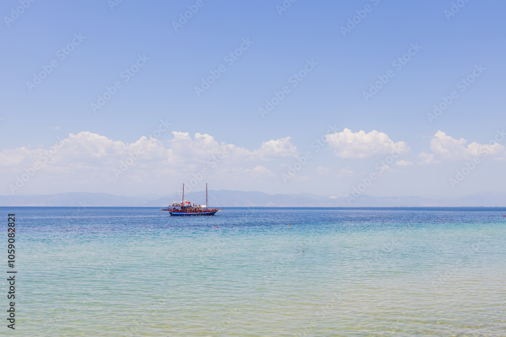 Large sailboat filled with passengers glides smoothly over the crystal-clear blue waters on a bright sunny day Large sailboat filled with passengers glides smoothly over the crystal-clear blue waters on a bright sunny day