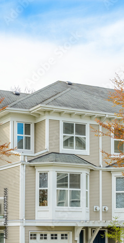 Top of grey stucco luxury house with shingle roof, red and yellow trees and nice windows in Summer in Vancouver, Canada, North America. Day time on June 2024.