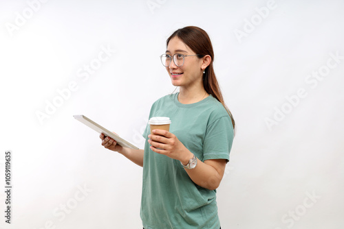 Smiling young asian college student woman using tablet computer, happy student woman in casual looking empty space standing while holding a cup of coffee over white background