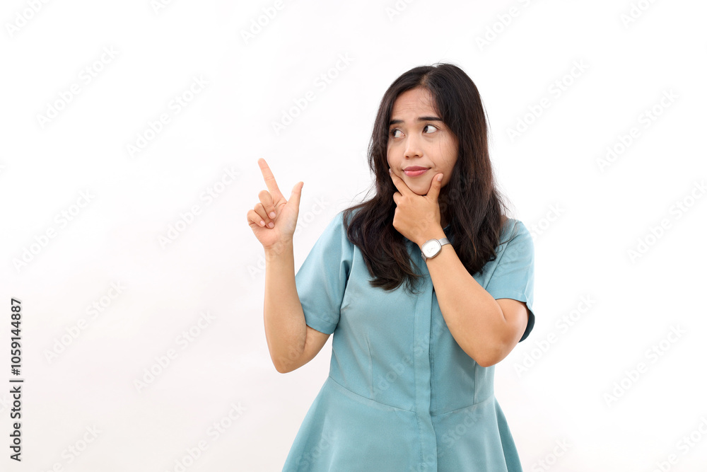 Hesitant young Asian woman holds chin purses lips has doubtful face expression points upwards shows promo ahead top sale promotion wears casual shirt poses against white background. Hesitant young Asian woman holds chin purses lips has doubtful face expression points upwards shows promo ahead top sale promotion wears casual shirt poses against white background.