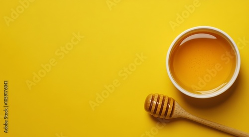 A bowl of honey with a wooden dipper on a bright yellow background