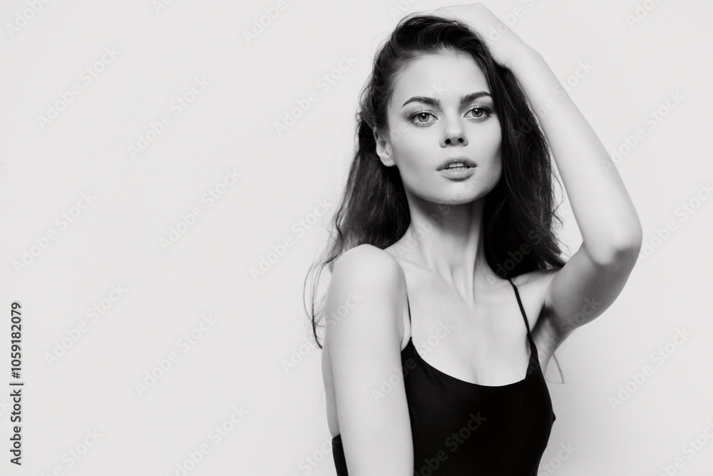 Fototapeta premium Young woman with long hair in a black top, striking a confident pose against a plain white background. Emphasis on beauty and self-expression.