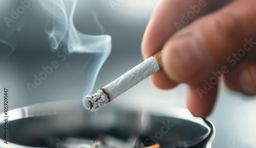 Hand Holding Lit Cigarette Over Ashtray