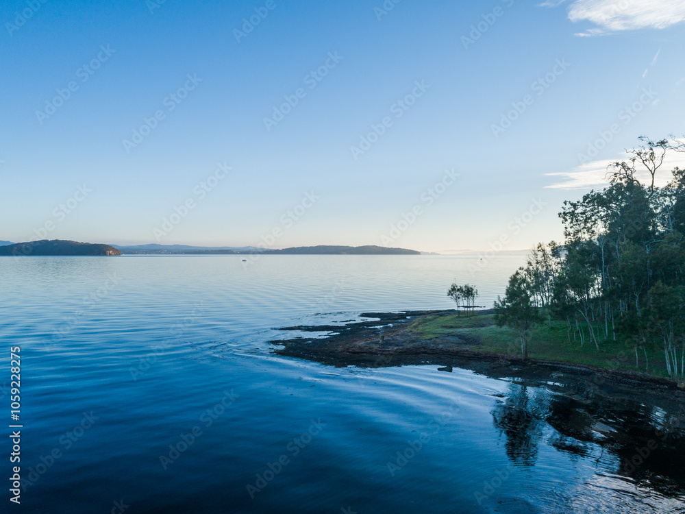 Trees on shoreline of lake with water reflecting blue sky on cold morning seen from aerial view Trees on shoreline of lake with water reflecting blue sky on cold morning seen from aerial view