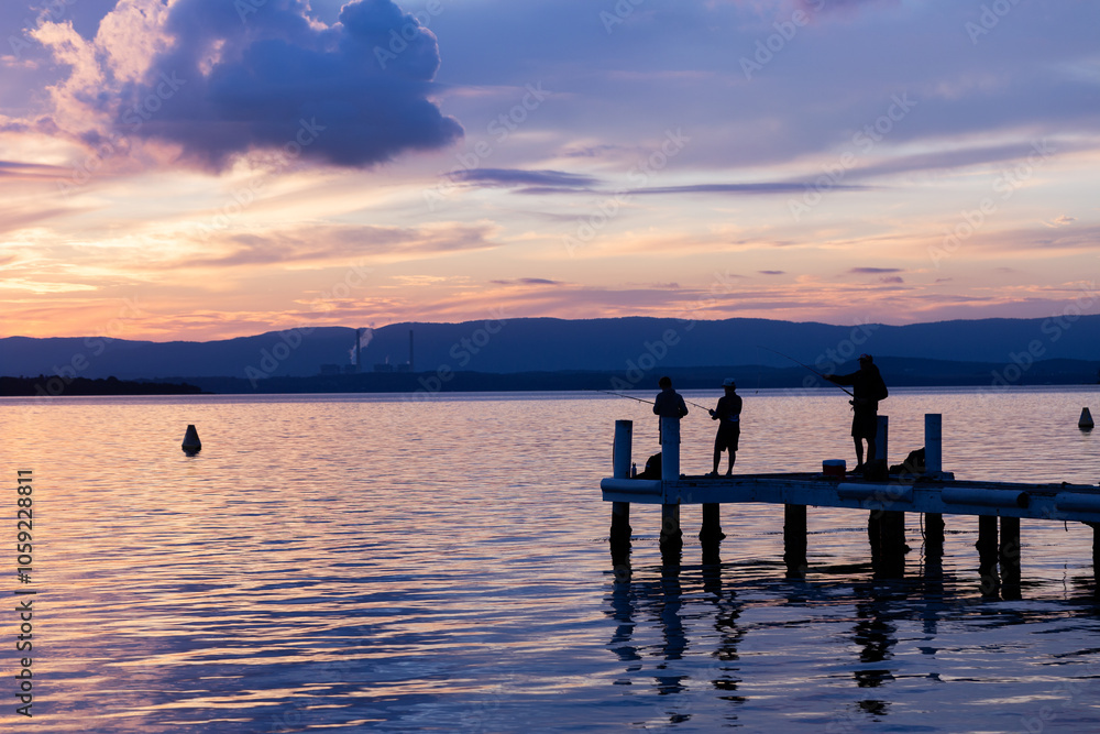 Family on jetty fishing together at sunset pastel purple colours of sky reflecting in water Family on jetty fishing together at sunset pastel purple colours of sky reflecting in water