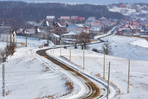Obraz na płótnie country road in winter through snow and village with houses covered with snow w salonie
