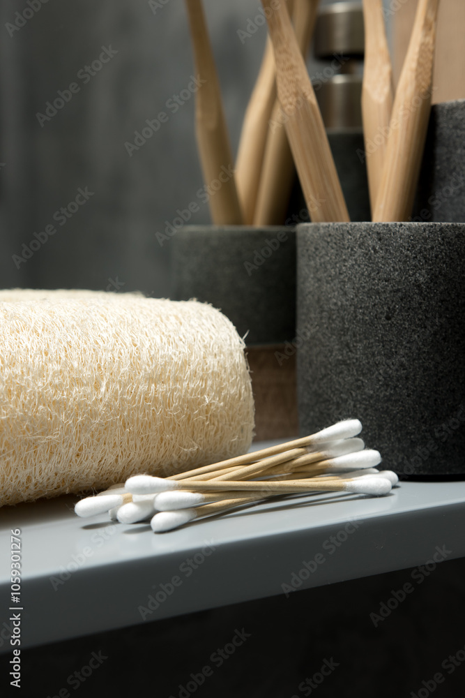Eco-friendly bathroom setup featuring bamboo toothbrushes in a holder, wooden cotton swabs, and a textured loofah on a reflective surface. Highlighting sustainable personal care products Eco-friendly bathroom setup featuring bamboo toothbrushes in a holder, wooden cotton swabs, and a textured loofah on a reflective surface. Highlighting sustainable personal care products