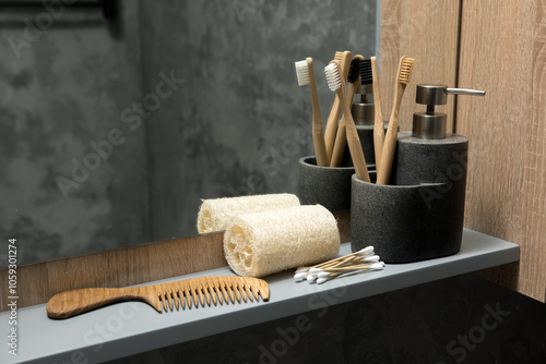 Bathroom countertop with bamboo toothbrushes, soap dispenser, wooden comb, and cotton swabs in stone containers. Eco-friendly and natural setup with a mirror and wooden cabinet in the background photo