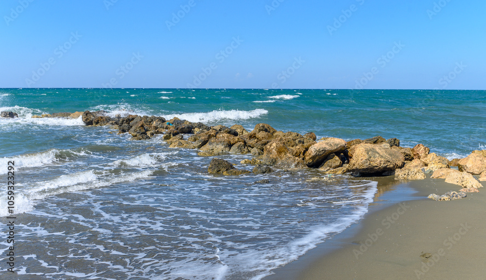 A tranquil day by the shoreline with gentle waves lapping at rocky outcrops under a clear blue sky A tranquil day by the shoreline with gentle waves lapping at rocky outcrops under a clear blue sky