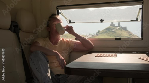 Woman traveler on campervan drinks tea or coffee while sitting near window.