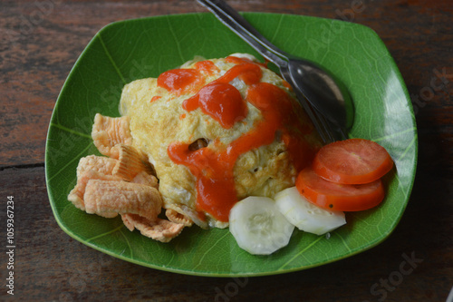 Nasi goreng or Indonesian fried rice topped with omelette called dadar telur padang with kropek or crackers, cucumber and tomatoes