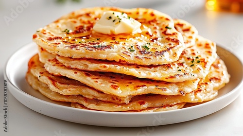  White plate with stacked pancakes and butter on top, served with orange juice in the background