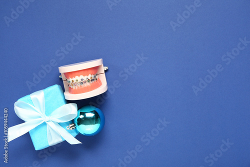 Model of jaw with dental braces, Christmas gift and ball on blue background photo