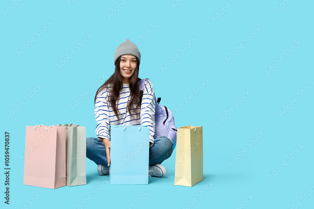 Fashionable young Asian woman in stylish jeans with shopping bags sitting on blue background Fashionable young Asian woman in stylish jeans with shopping bags sitting on blue background