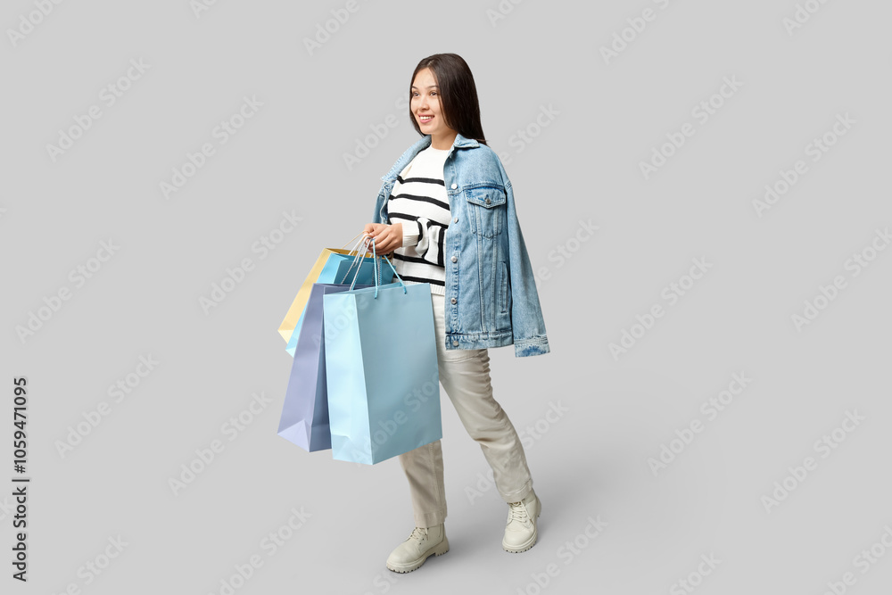 Fashionable young Asian woman in denim clothes with shopping bags on grey background Fashionable young Asian woman in denim clothes with shopping bags on grey background