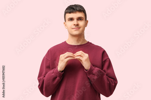 Young deaf mute man using sign language on pink background photo