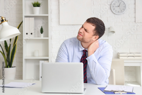 Businessman suffering from neck pain at table in office