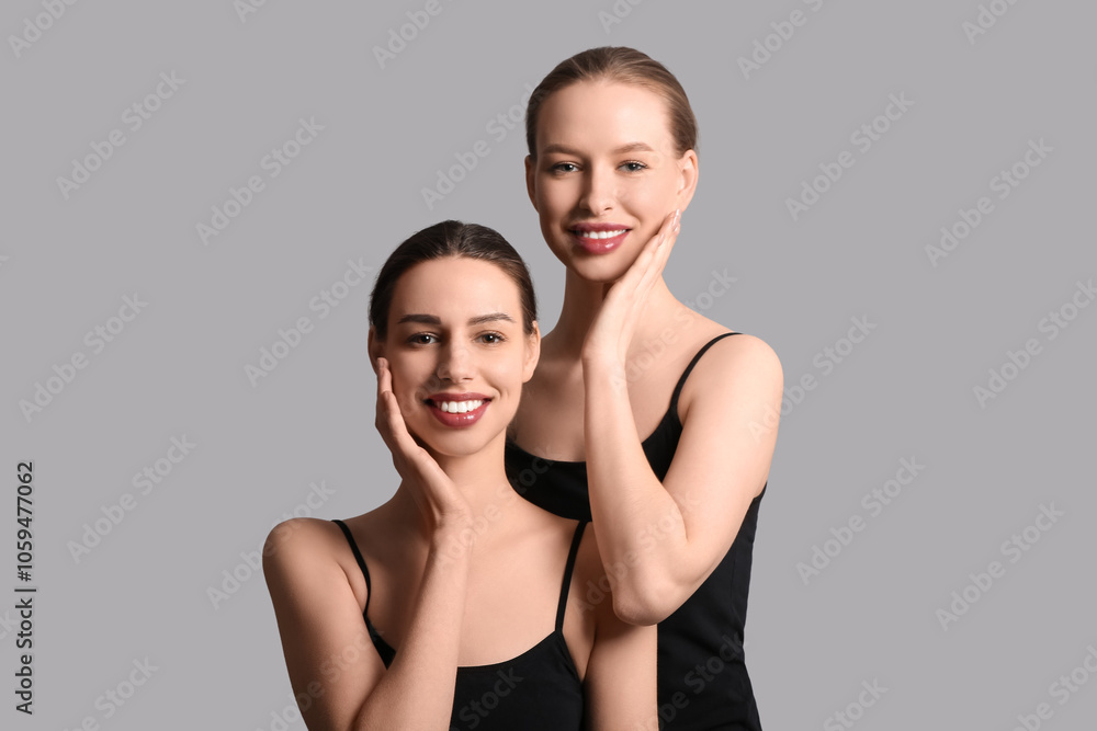 Smiling young sisters on grey background Smiling young sisters on grey background