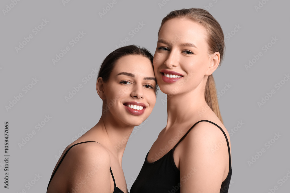 Smiling young sisters on grey background Smiling young sisters on grey background