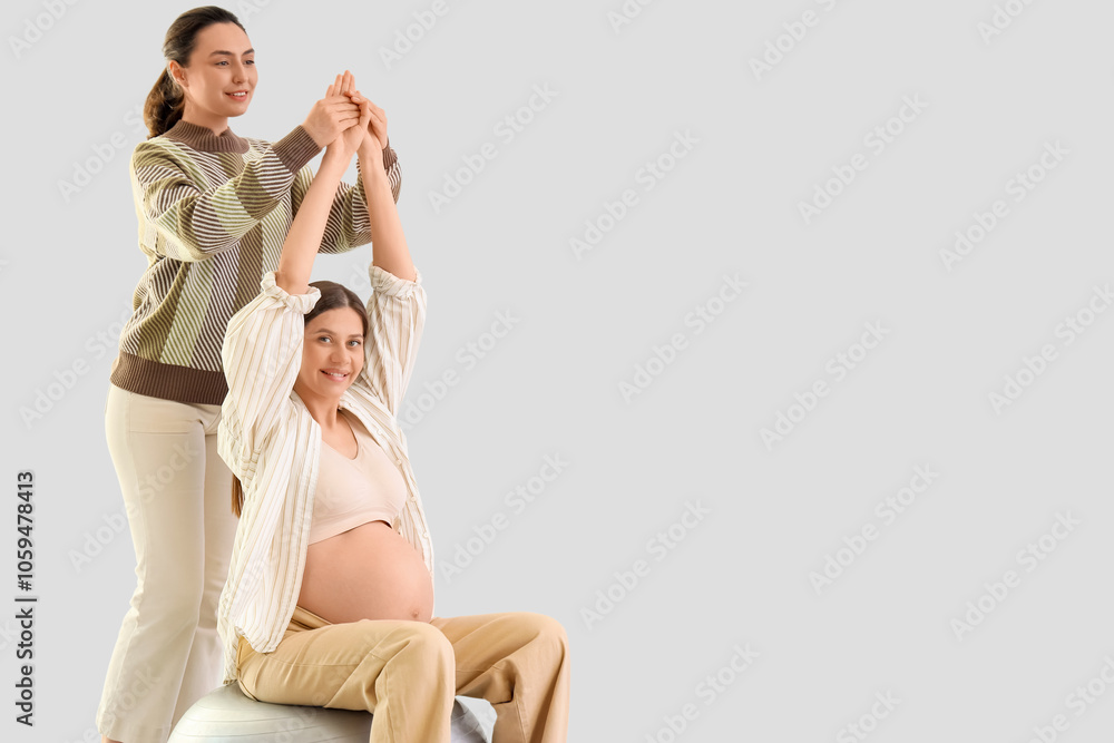 Young pregnant woman with doula training on fitball against light background Young pregnant woman with doula training on fitball against light background