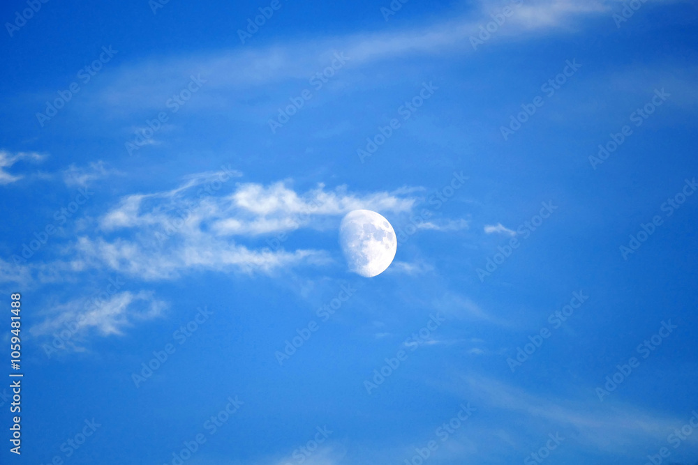close view of the moon during the day, full moon view of the moon on a blue and cloudy day,