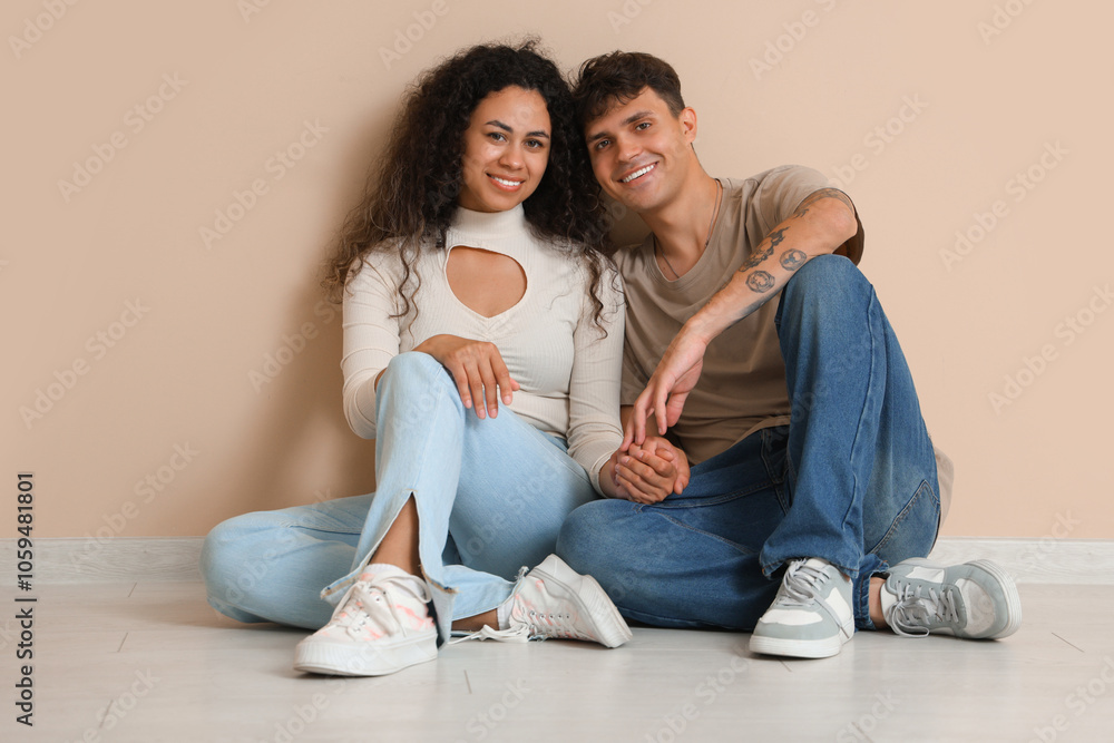 Young couple sitting on floor near beige wall in their new flat Young couple sitting on floor near beige wall in their new flat