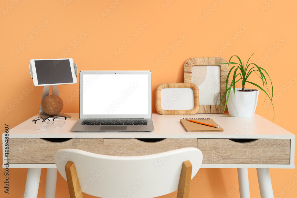 Fototapeta premium Stylish table with modern laptop and tablet near orange wall in room