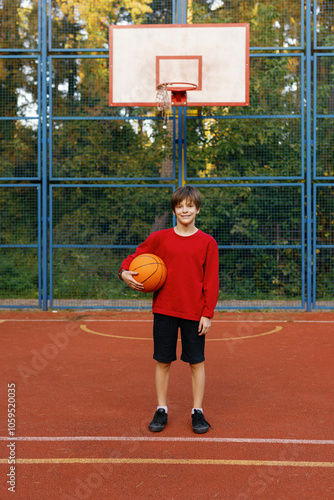 Kid posing with ball in front of basket on outdoor basketball court