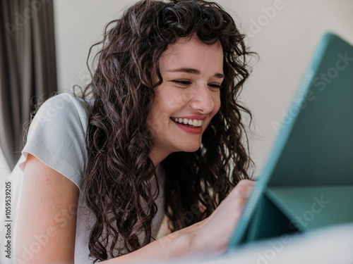 Curly Haired Young Woman Smiling While Using a Tablet at Home photo