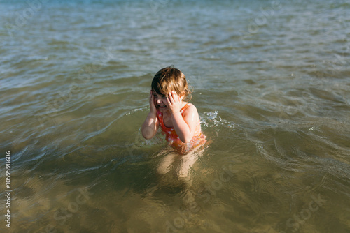 Young girl playing in the ocean holding her face. photo