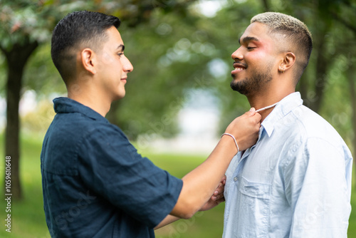 Young hispanic man fixing boyfriend's shirt collar in park photo