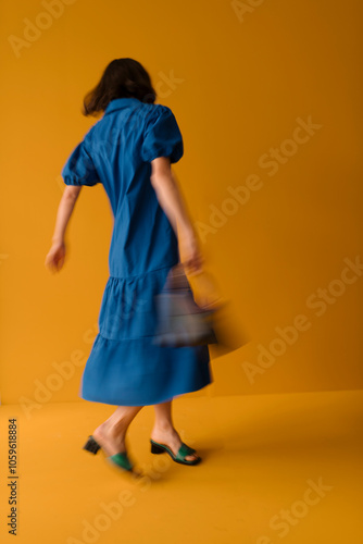 Woman in Blue Dress Twirls on Vibrant Orange Background photo