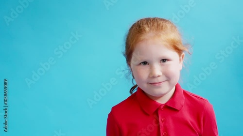 Cheerful redhead child nods her head in agreement against a bright blue background in a playful moment of innocence and joy