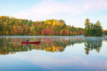 Senior man paddling a red wooden canoe on a beautiful northern Minnesota lake with a small island at dawn during autumn