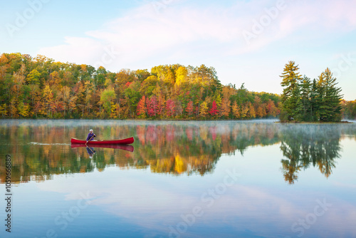 Senior man paddling a red wooden canoe on a beautiful northern Minnesota lake with a small island at dawn during autumn