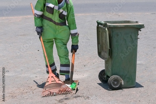 Street cleaning, male municipal worker in fluorescent uniform collecting street rubbish to dumpster. Labor law, labor rights for migrants, refugee, unskilled labor. photo