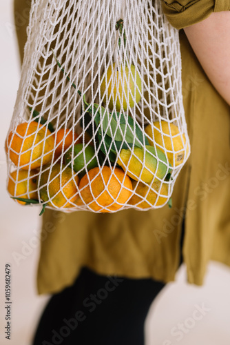 Person carrying a mesh bag with fresh oranges and limes photo