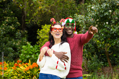 Christmas time, embracing outdoors, joyful multiracial couple wearing festive glasses photo