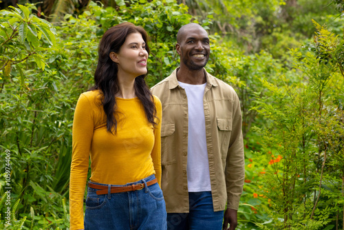 Smiling multiracial couple walking together in lush green garden, enjoying nature photo