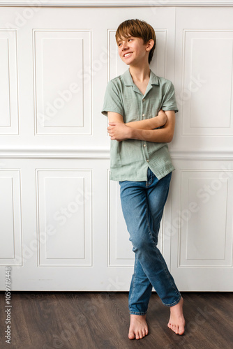 Natural light portrait of a young teen boy in blue jeans casually leaning against a white, wood paneled wall photo