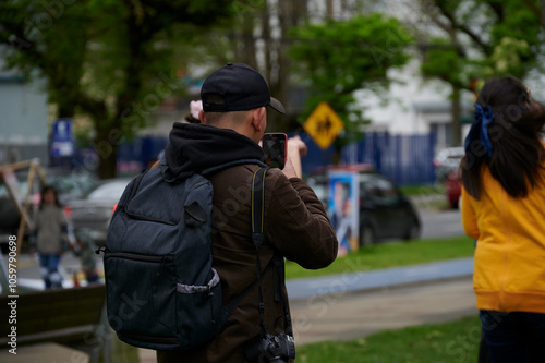 Wallpaper Mural Photographer filming with a cell phone to people at a festival in a large man's park with black cap and coffee jacket in black wool lines around cars
 Torontodigital.ca