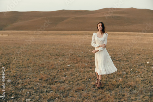 Woman standing in white dress in open field with mountains in background, serene travel beauty in nature scene