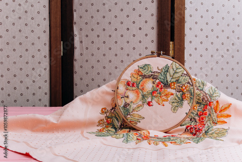 An embroidery hoop with a bright floral pattern is shot close-up against a pale pink background. Do-it-yourself aesthetic installation. photo