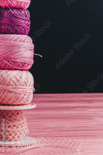 A collection of knitting skeins stacked on top of each other on a pastel pink wooden surface with a black background behind.