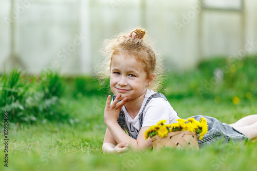 Beautiful curly little girl lying on green grass lawn at the backyard with yellow dandellions photo