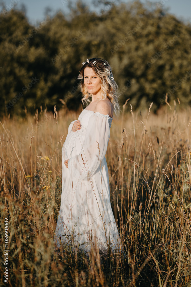 Obraz premium A young expectant mother in the third trimester of pregnancy in a white dress against the background of a natural landscape. The concept of future motherhood.