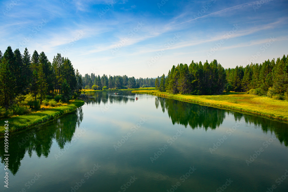Fototapeta premium 2024-09-10 THE DESCHUTES RIVER WITH A BEAUTIFUL REFLECTION IN THE WATER AND A GRASS AND TREE LINED SHORE IN SUNRIVER OREGON