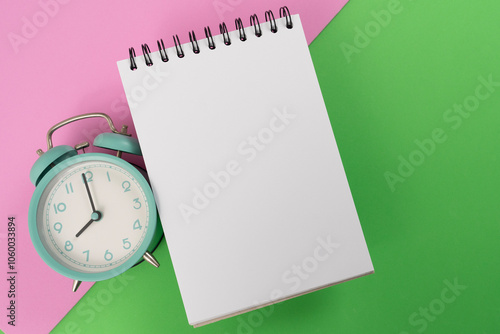 Retro alarm clock and notebook on pink and green table background, vintage style, flat lay