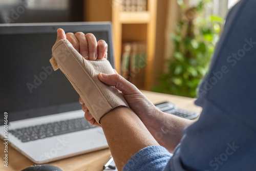 Person Using Wrist Brace For Hand Injury Due To Remote Computer Work, Showing Carpal Tunnel Syndrome, Tendonitis, And Hand Tension From Repetitive Strain In Home Office Setting photo